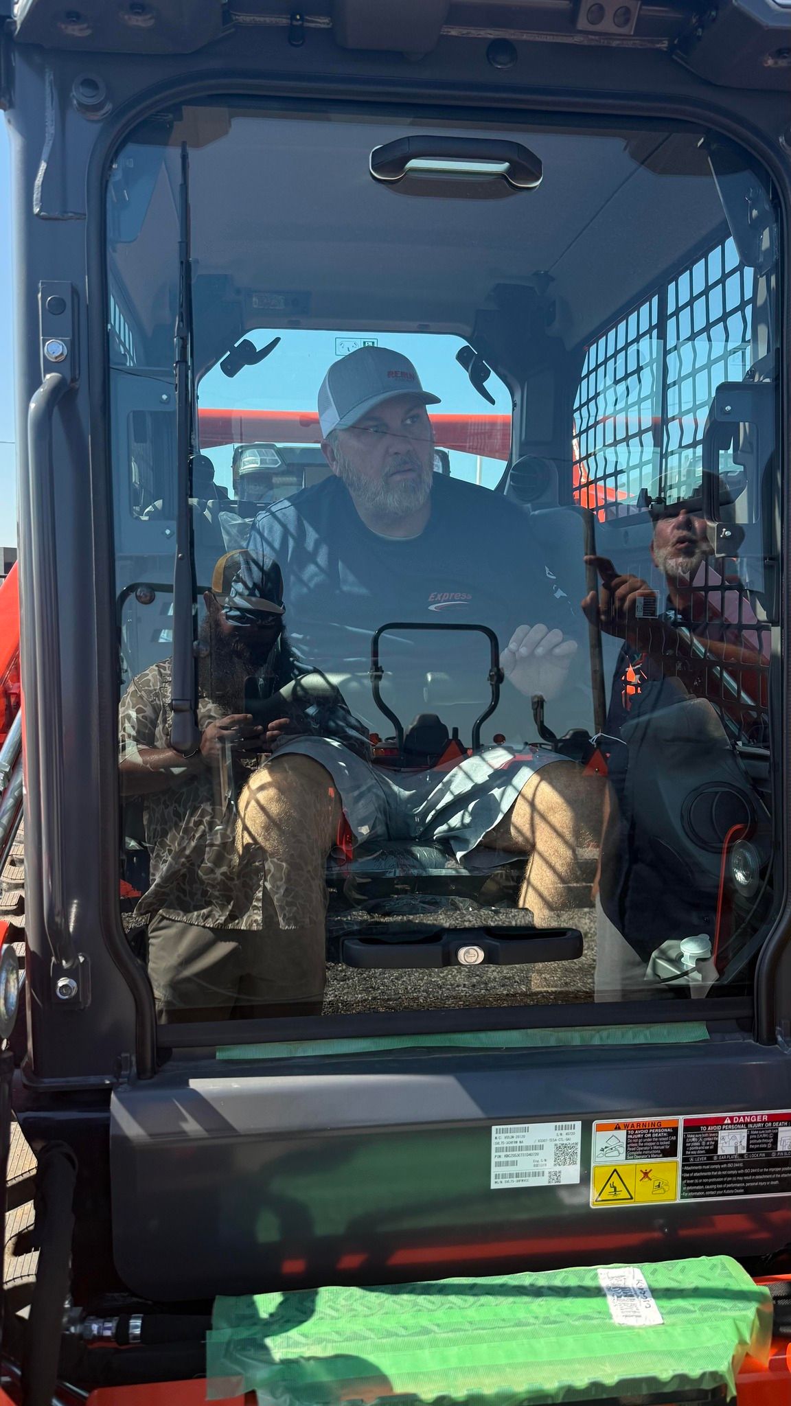 Man sitting inside a skid steer cab, wearing a baseball cap.