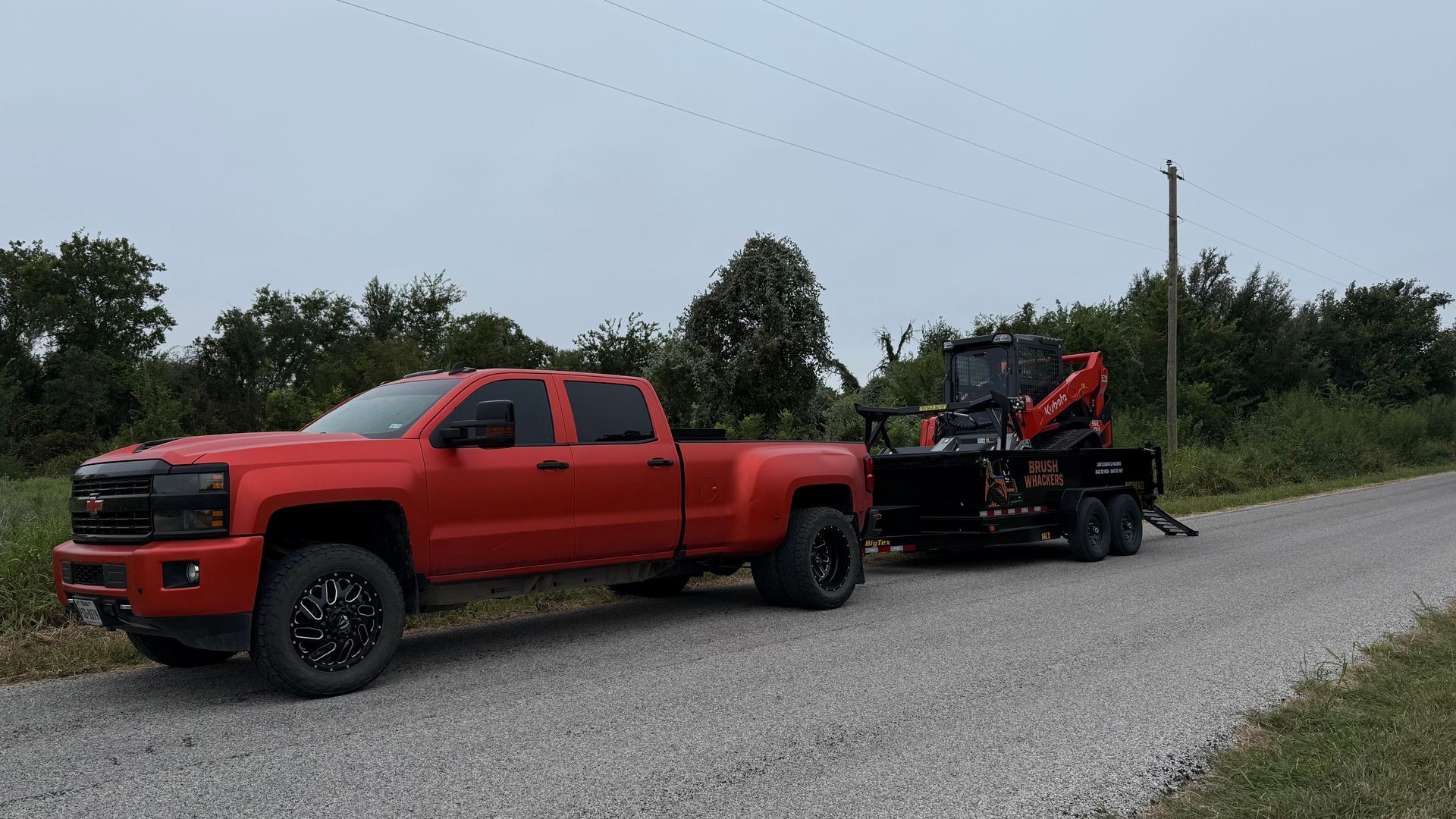Red truck towing a trailer with a compact excavator on a gravel road.