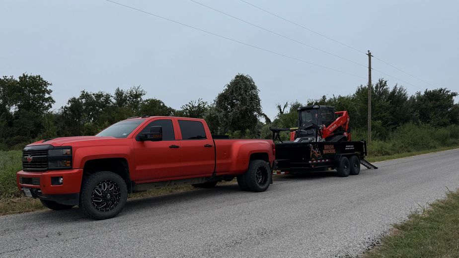 Red truck towing a trailer with a compact excavator on a gravel road.