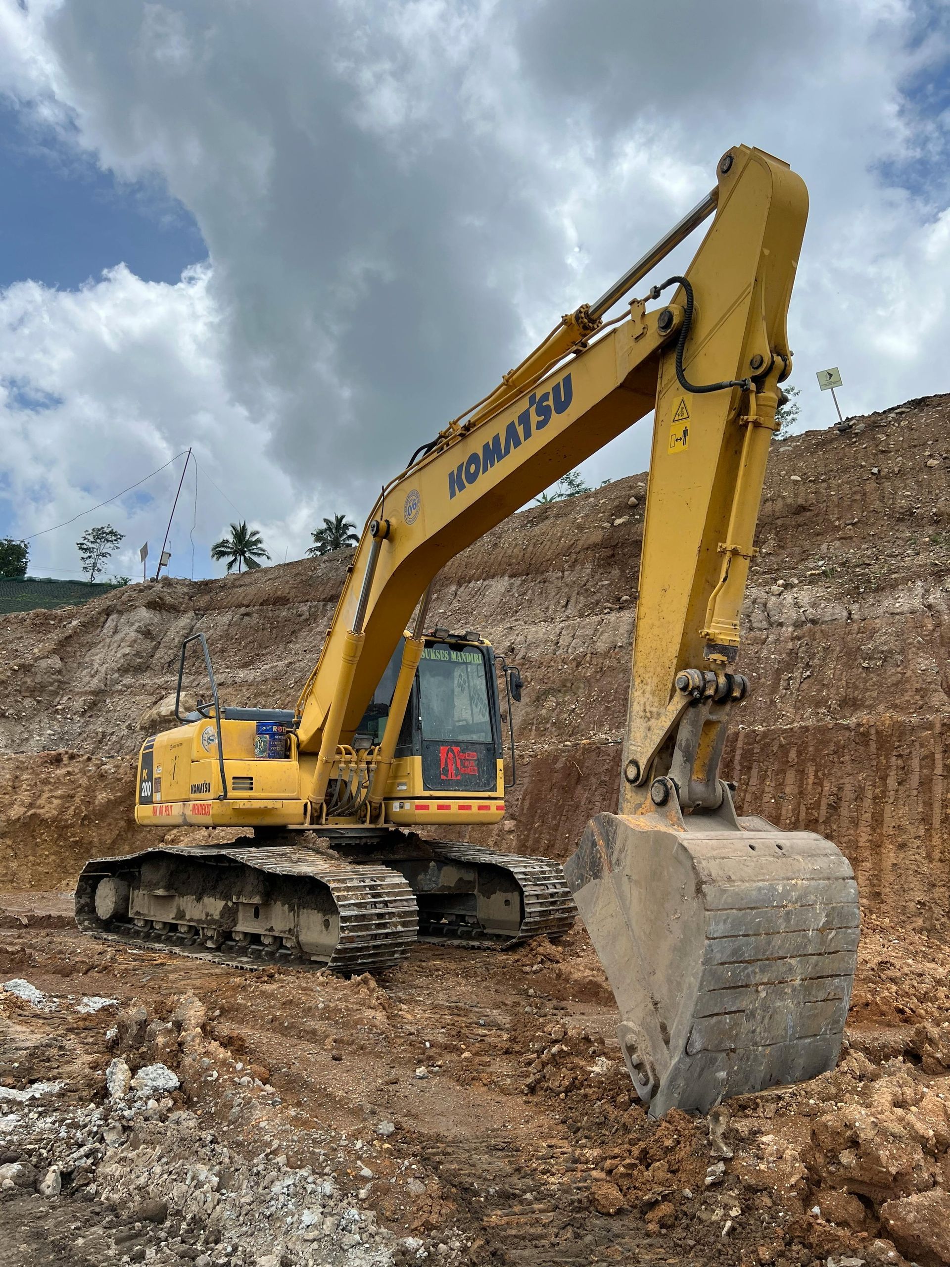 Yellow Komatsu excavator digging earth on a hillside under a cloudy sky.