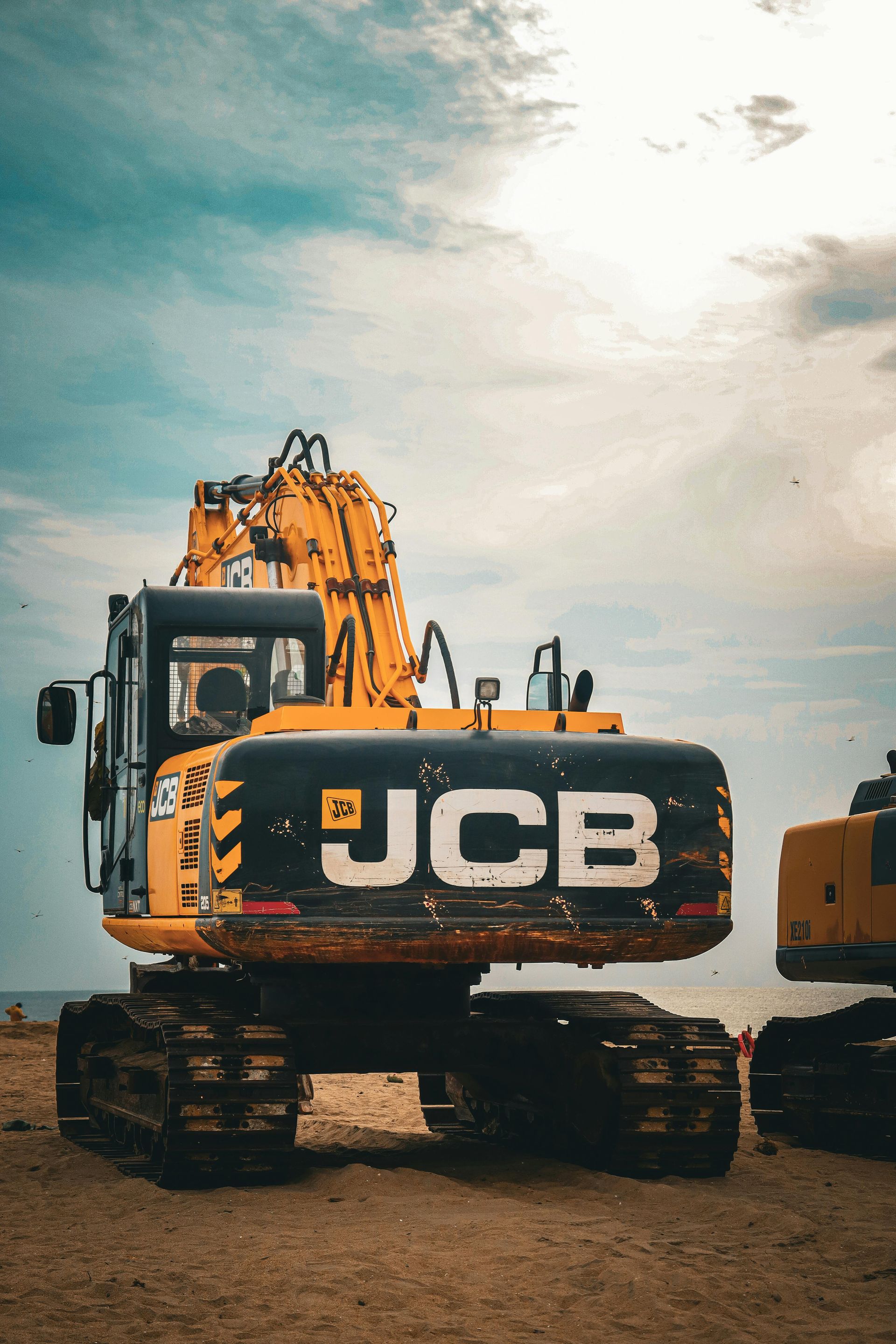 Yellow and black JCB excavator on a construction site with a cloudy sky in the background.