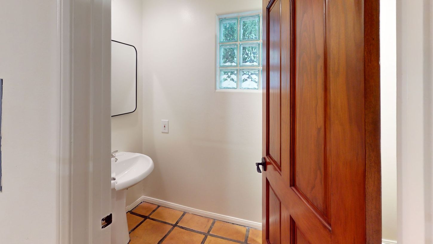 Small bathroom with a brown wooden door, white sink, and tiled floor.