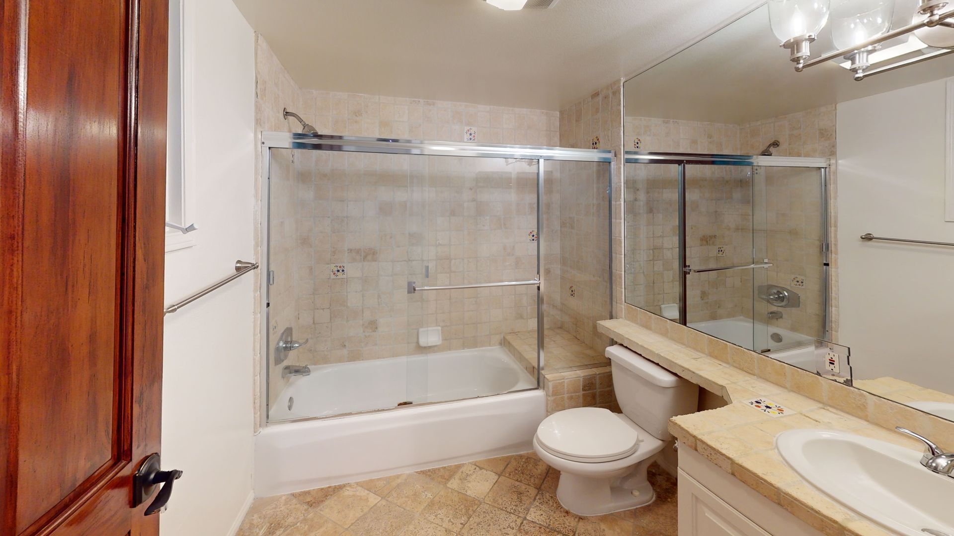 Bathroom with beige tile, white toilet and sink, shower, and a large mirror.