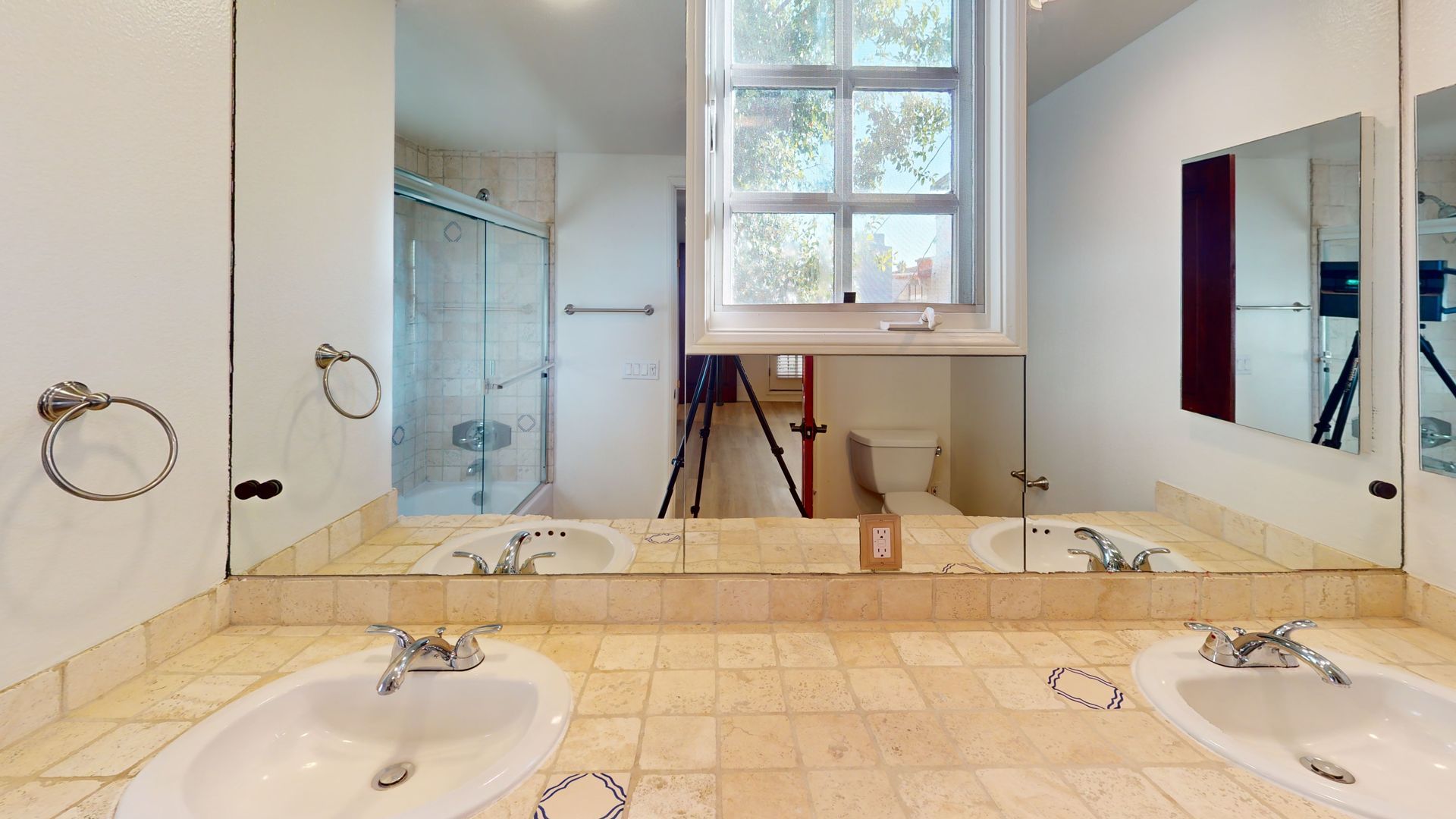 Bathroom with two sinks, a shower, and a window. Beige tile, mirrors, and white walls.