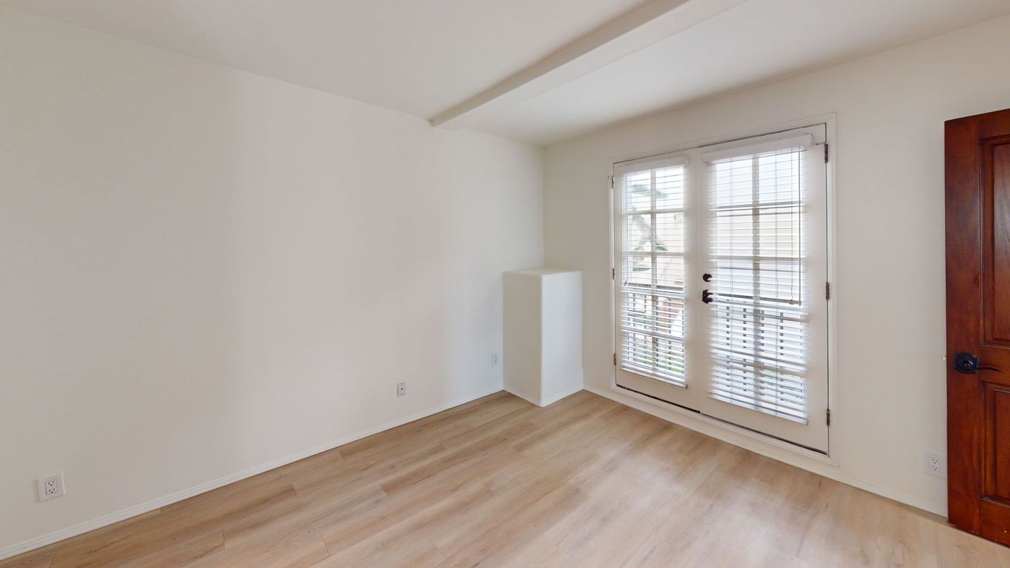 Empty room with light wood floors, white walls, and French doors.