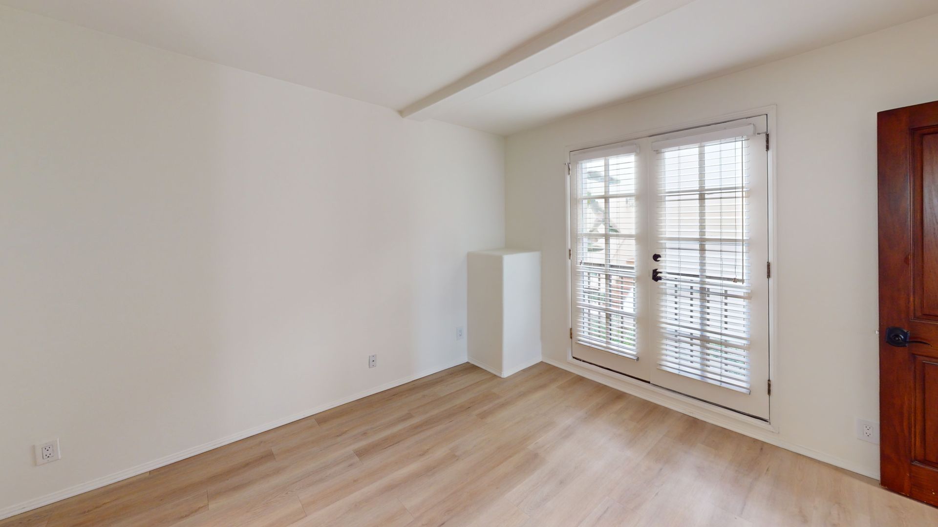 Empty room with light wood floors, white walls, and French doors.