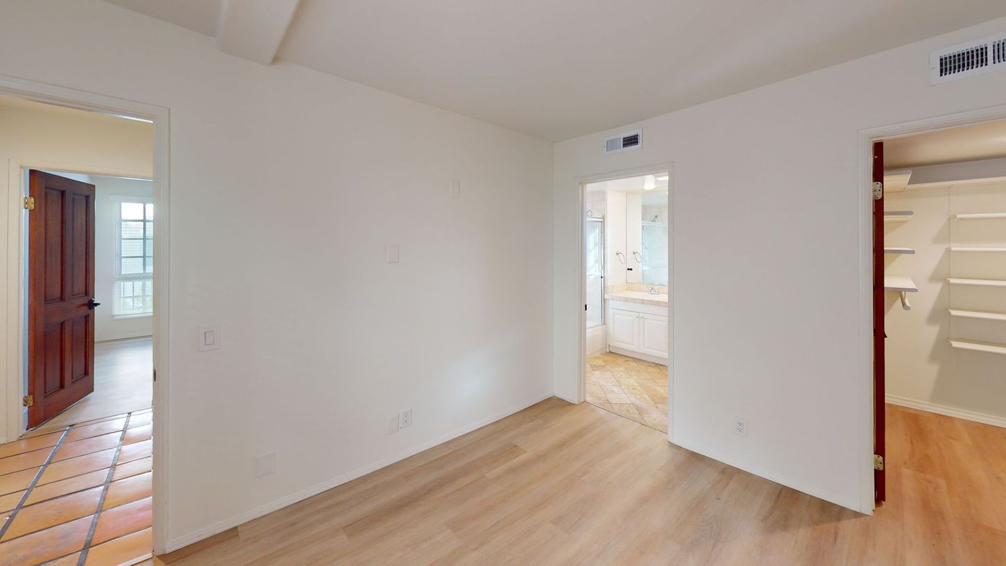 Empty room with light wood floors, doorways to bathroom, closet, and another room with terra cotta tile.