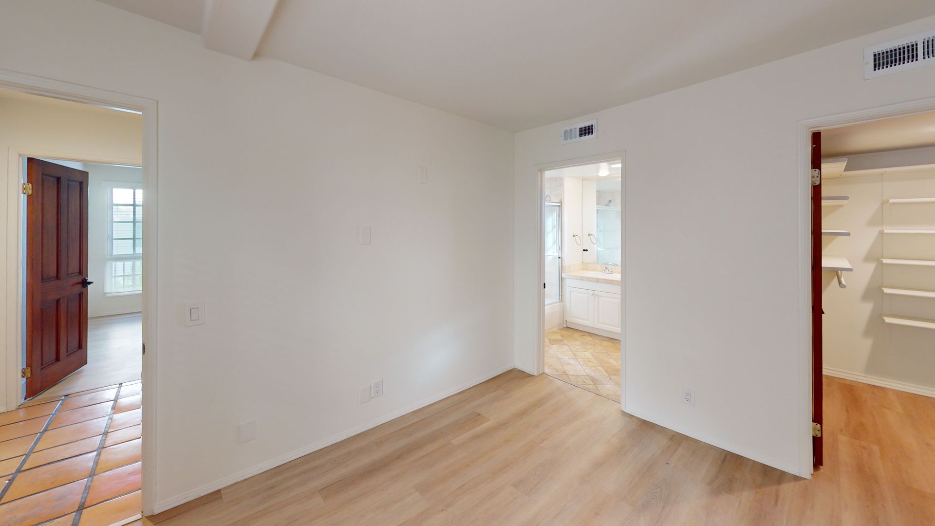 Empty room with light wood floors, doorways to bathroom, closet, and another room with terra cotta tile.