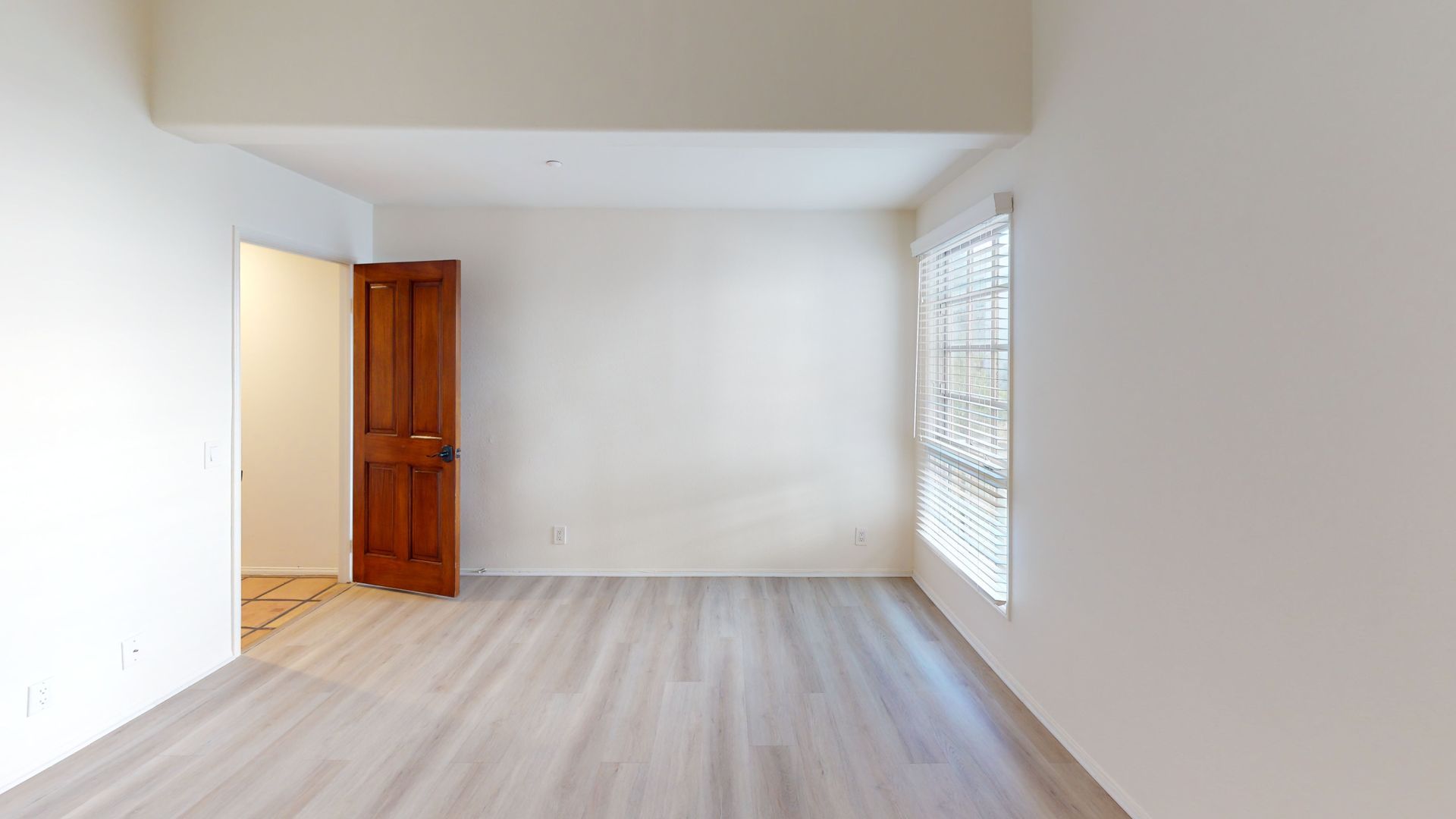 Empty room with wooden door, window, and light gray flooring.