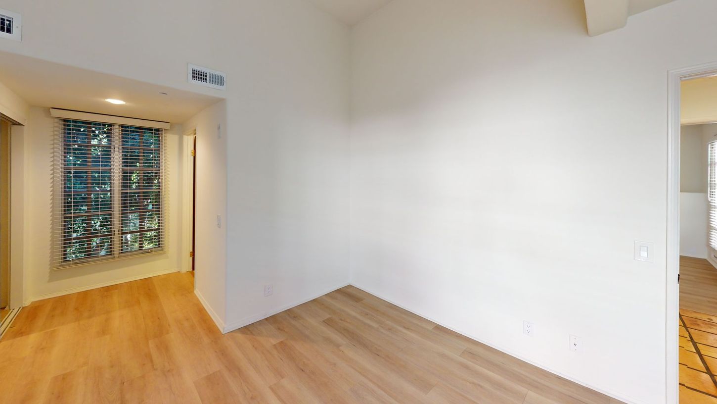 Empty room with wood floors and white walls. Window with trees visible.