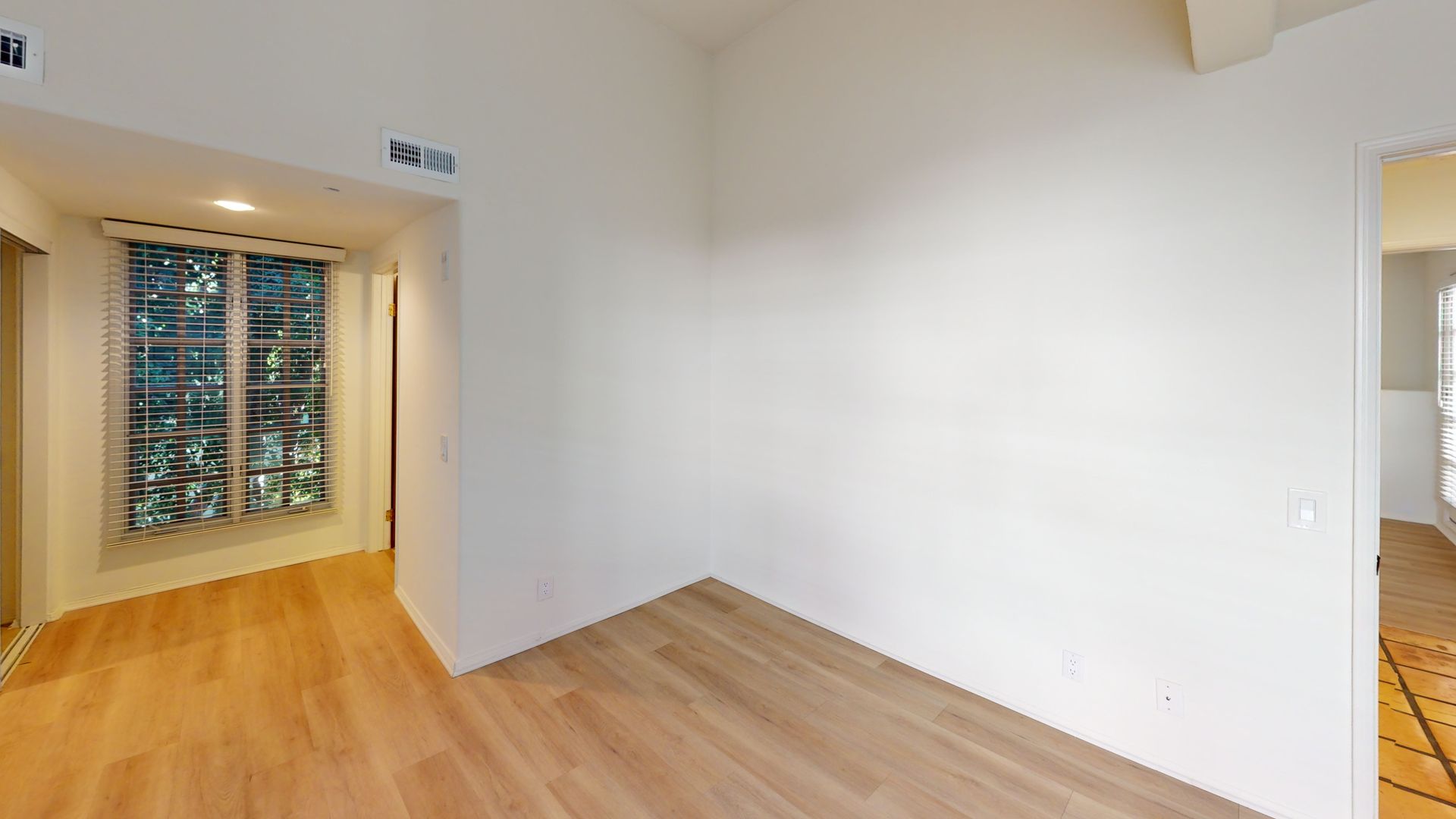 Empty room with wood floors and white walls. Window with trees visible.