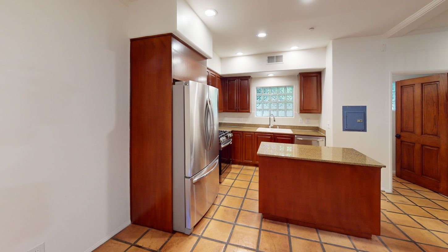 Kitchen with brown cabinets, stainless steel refrigerator, and island on tiled floor.