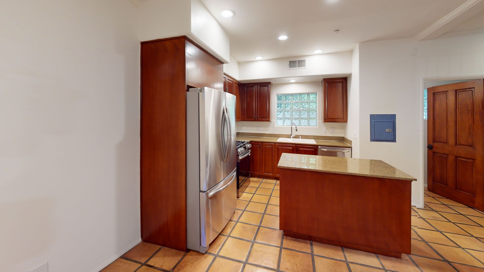 Kitchen with brown cabinets, stainless steel refrigerator, and island on tiled floor.