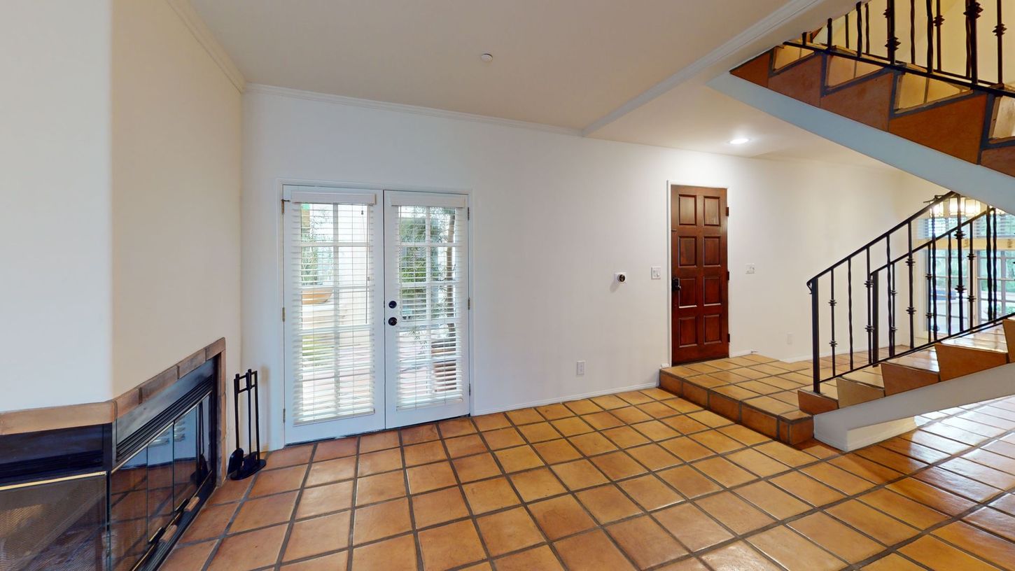 Interior with terracotta tile floor, white walls, double doors to a patio, and staircase.