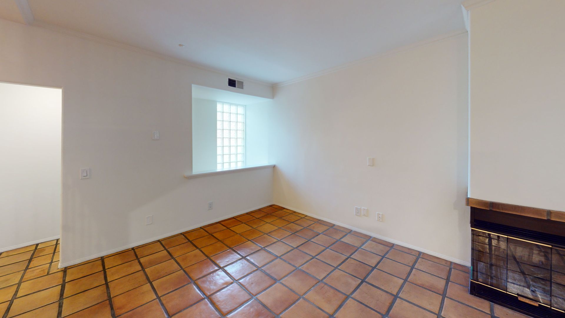 Empty room with terracotta tile floor, window with glass blocks, and fireplace.