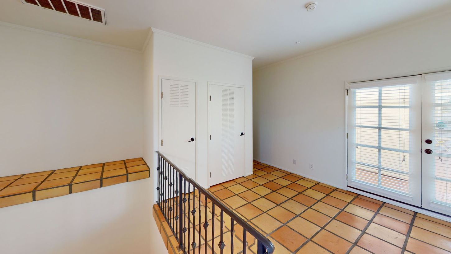 Hallway with white walls, closet, and terracotta tile floor, leading to French doors.