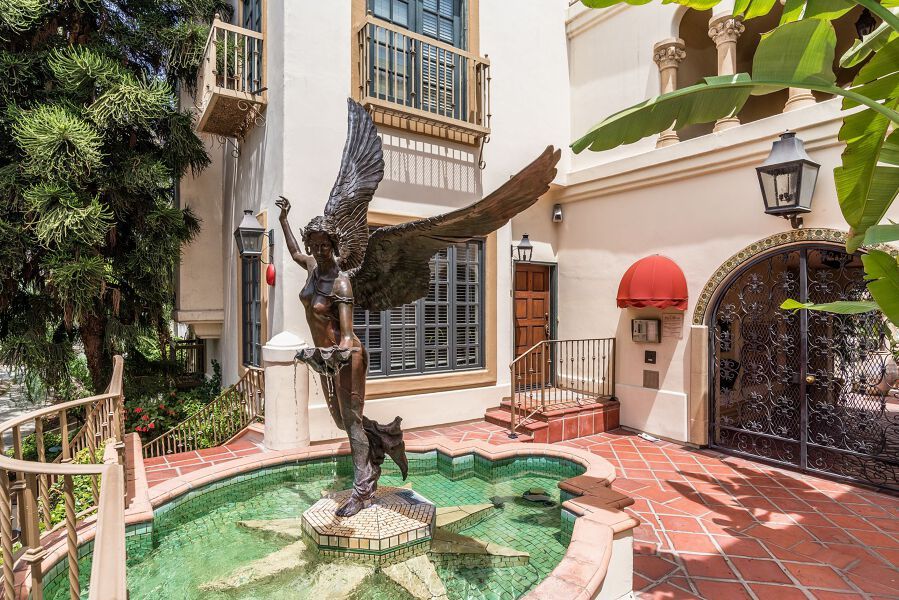 Courtyard with bronze angel statue in a pool; arched doorway with red awning, ornate gate.