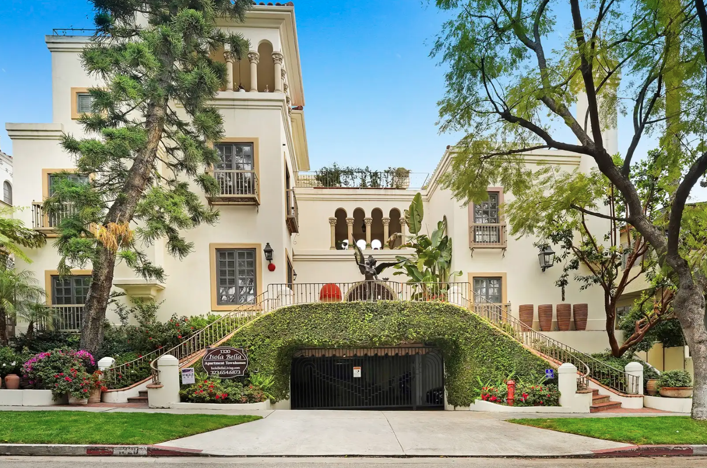 Beige multi-story building with arched windows, a green garage entrance, and lush landscaping.