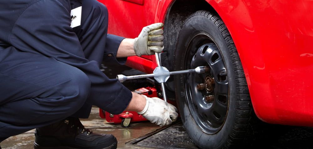A Mechanic in Blue Overalls Changing a Tire on A Red Car — Autoplus Picton in Picton, NSW