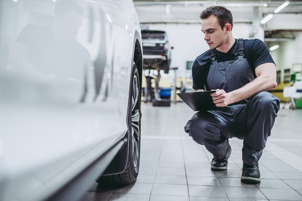 Mechanic in Grey Overalls Inspecting a Car Wheel with A Clipboard — Autoplus Picton in Picton, NSW