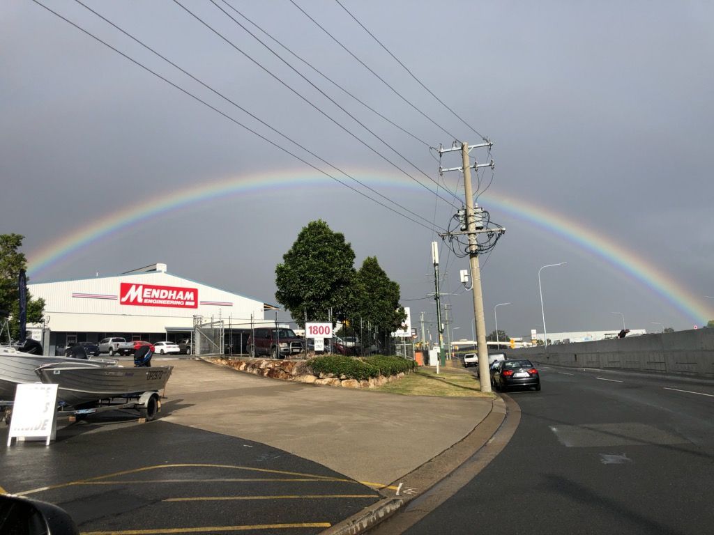 A rainbow is visible over a parking lot in front of a building — Brisbane, QLD — Mendham Engineering Pty Ltd