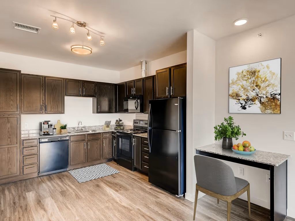 Modern kitchen with dark wood cabinets, stainless steel appliances, and a small dining area with a chair and fruit bowl.