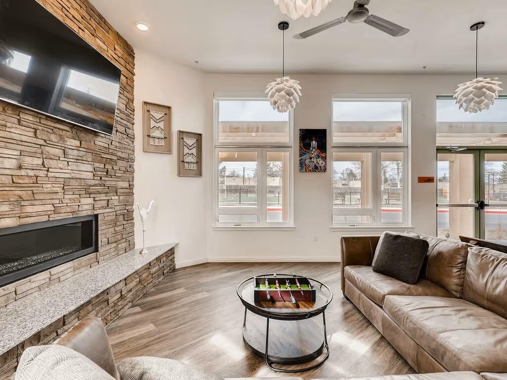 A modern, well-lit living area with a stone fireplace, leather sofa, wood floors, and a foosball coffee table.