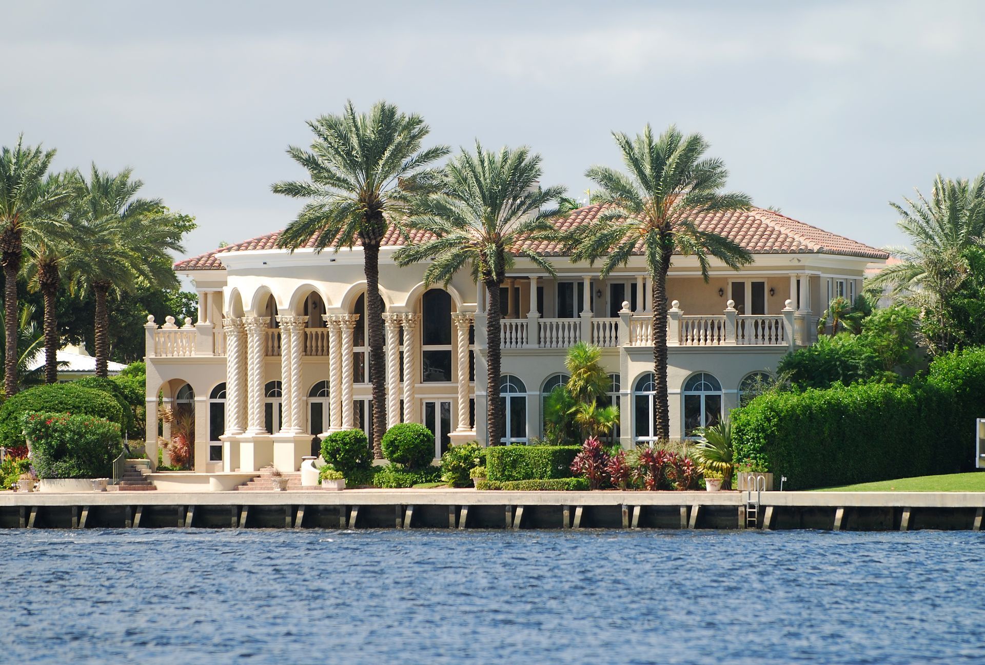 A luxury Mediterranean-style mansion with arched columns and palm trees on a waterfront property.