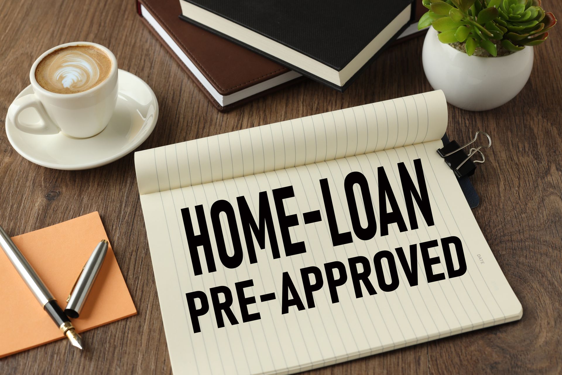 Notepad reading “Home Loan Pre-Approved” on a desk with coffee and office items.