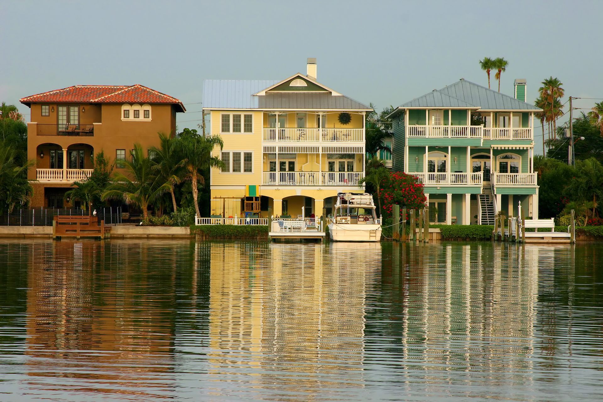 Three colorful waterfront houses with boats, reflecting in calm water.
