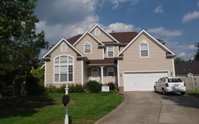 Two-story beige house with a white garage door and a white minivan parked in the driveway on a sunny day.