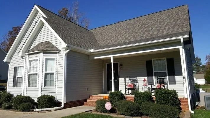 Light gray house with a dark gray roof, white trim, and a small porch, set against a blue sky.