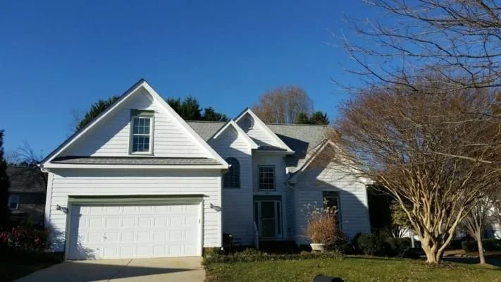 White house with a gabled roof and attached garage on a sunny day; bare tree in the front yard.