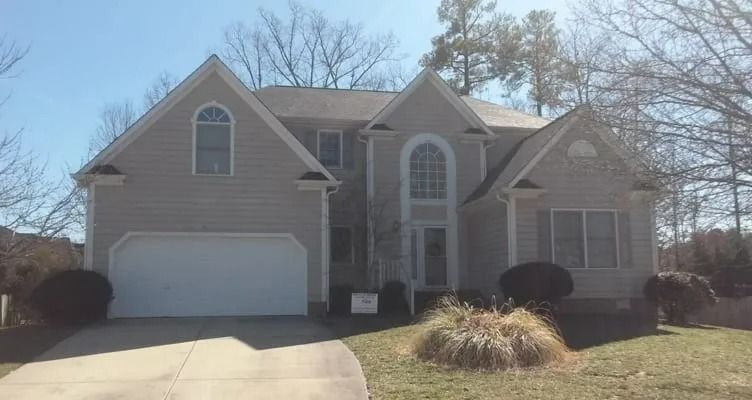 Two-story beige house with a white garage door and a curved driveway on a sunny day.