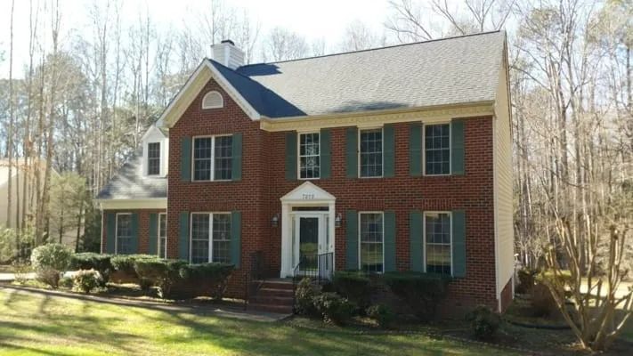 Two-story red brick house with green shutters, white trim, and a white front door, set amongst bare trees.