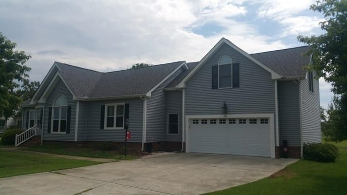 A two-story gray house with a white garage door and a curved window. The house is on a green lawn with a concrete driveway.