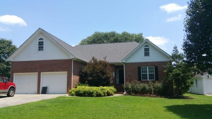 Brick house with two-car garage, white trim, and a green lawn under a blue sky. Landscaping frames the front door.