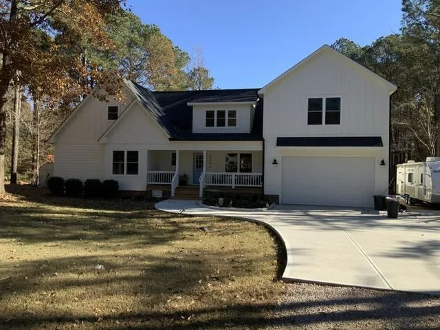 White two-story house with a dark roof, garage, and porch. A driveway curves in front of the house, with a camper parked on the side.