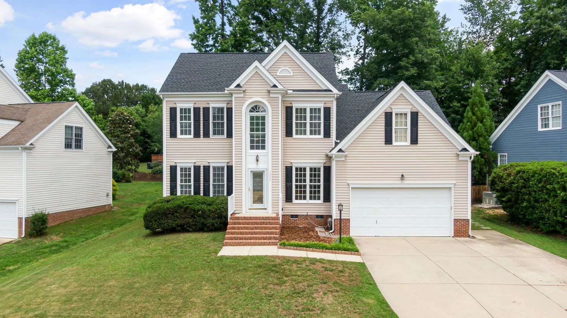 Two-story beige house with black shutters, a gray roof, and a white garage door, set on a green lawn.