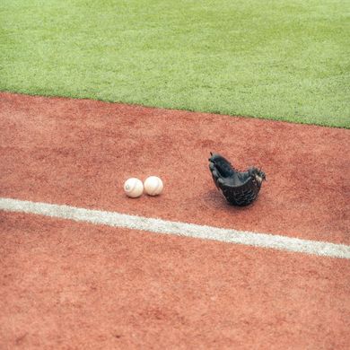 Baseball glove with ball on green grass, with blurred baseballs in the background.