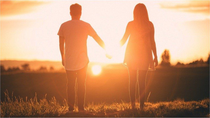 a man and a woman are holding hands in a field at sunset .