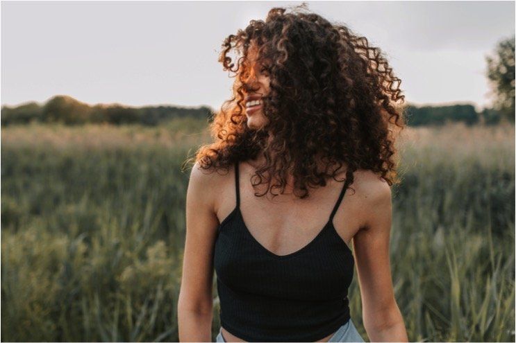 a woman with curly hair is standing in a field wearing a black tank top .