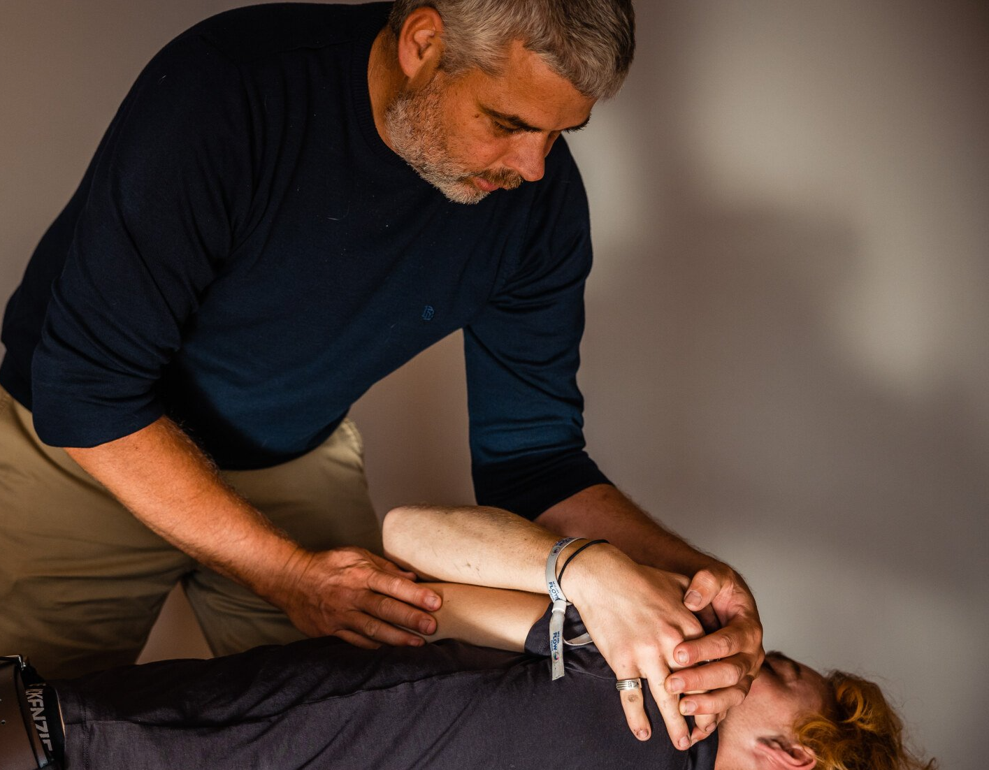 a man is stretching another man 's arm while laying down