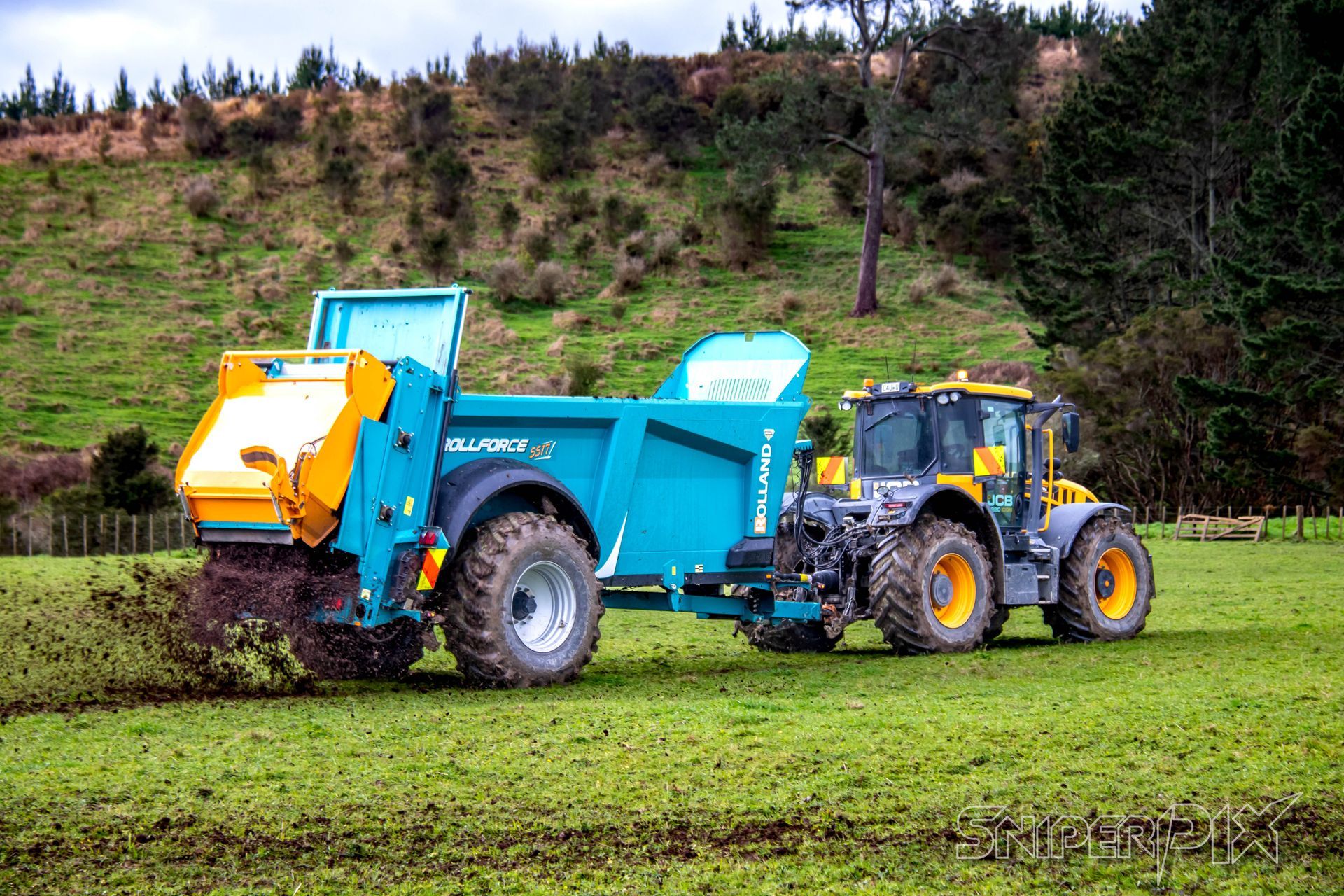 A tractor pulling a teal manure spreader spreading fertilizer on a green field. A tractor pulling a teal manure spreader spreading fertilizer on a green field.