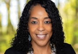 A woman is sitting at a desk with a laptop and a vase of flowers.