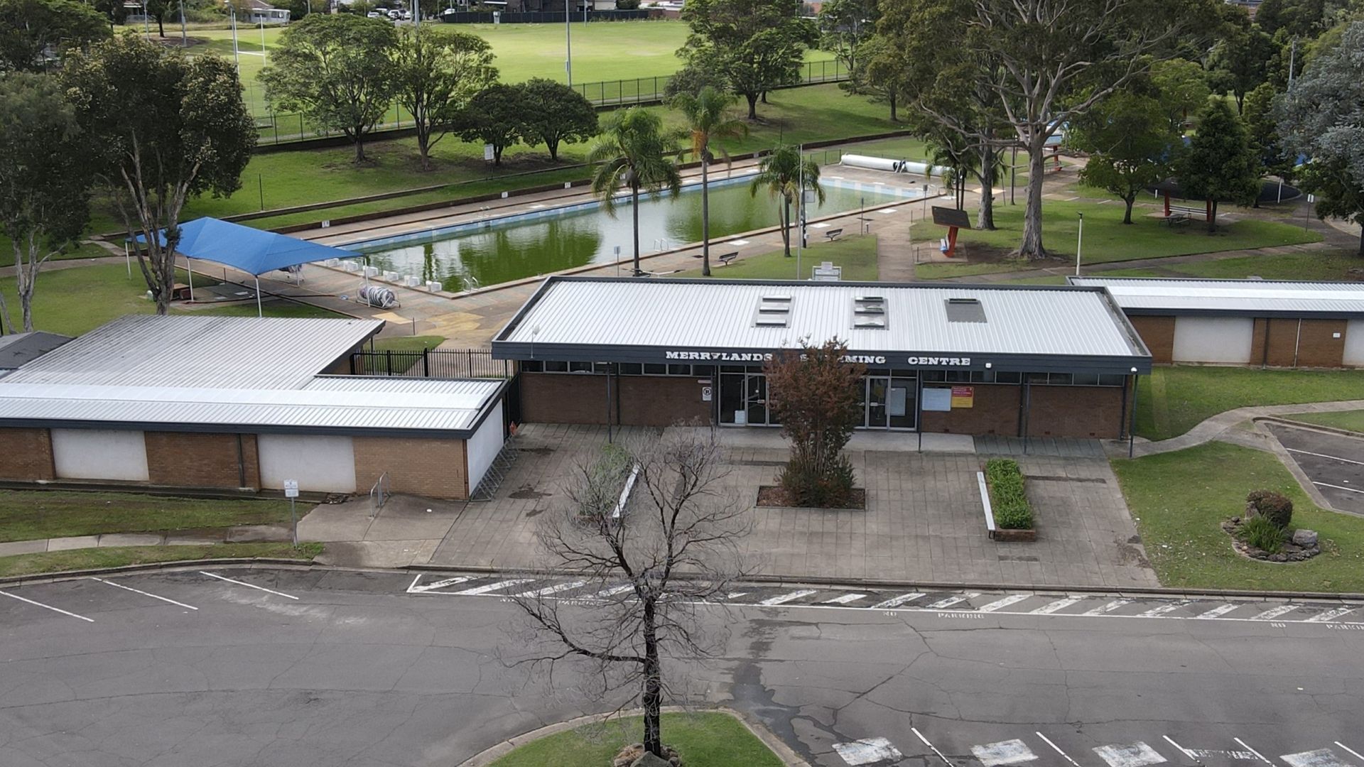 An aerial view of a building in a park with a pool in the background.