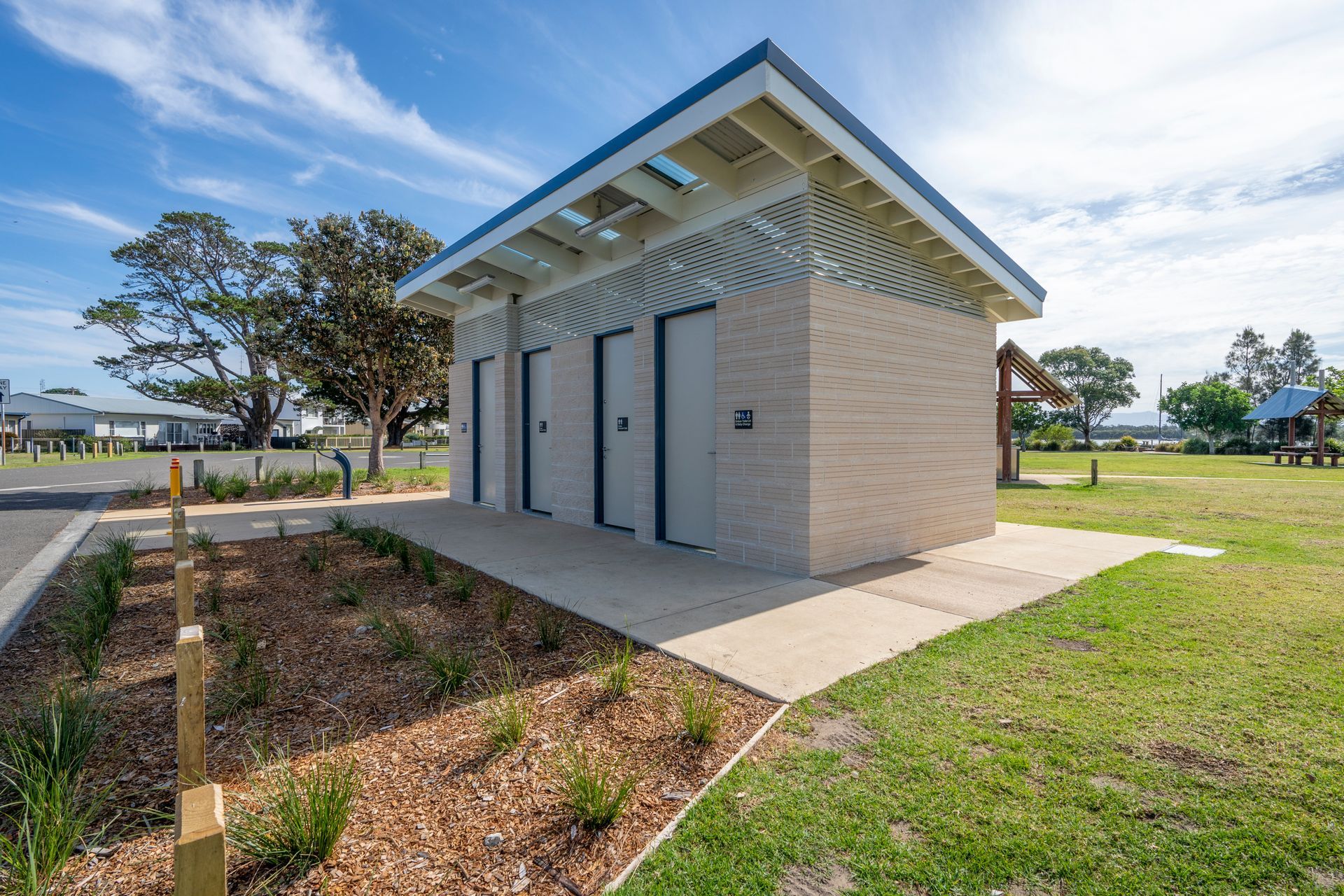 A brick building with a blue roof is sitting in the middle of a grassy field.