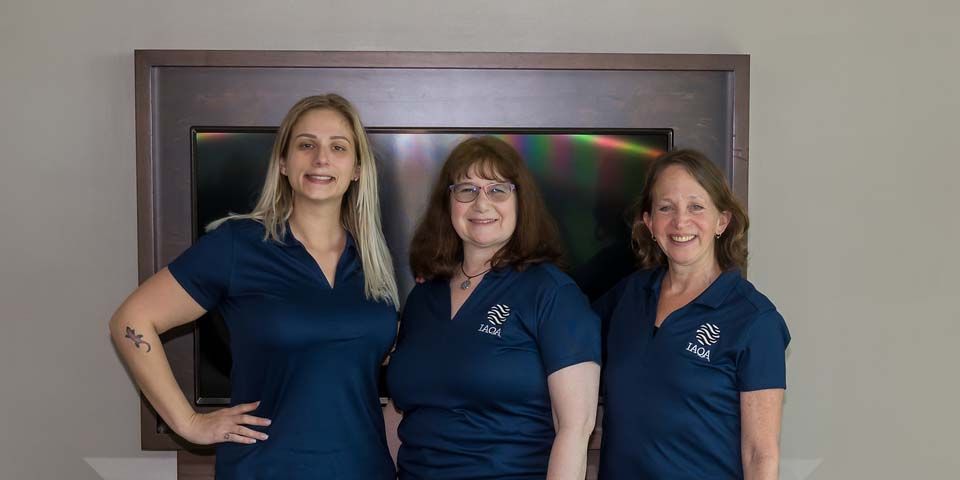 Three women are posing for a picture in front of a television.