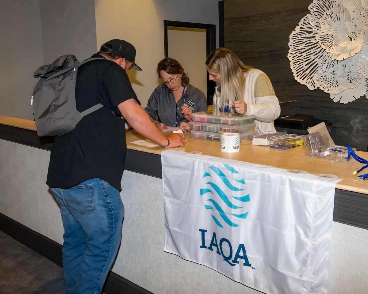 A man with a backpack is standing in front of a table with a banner that says iaqa