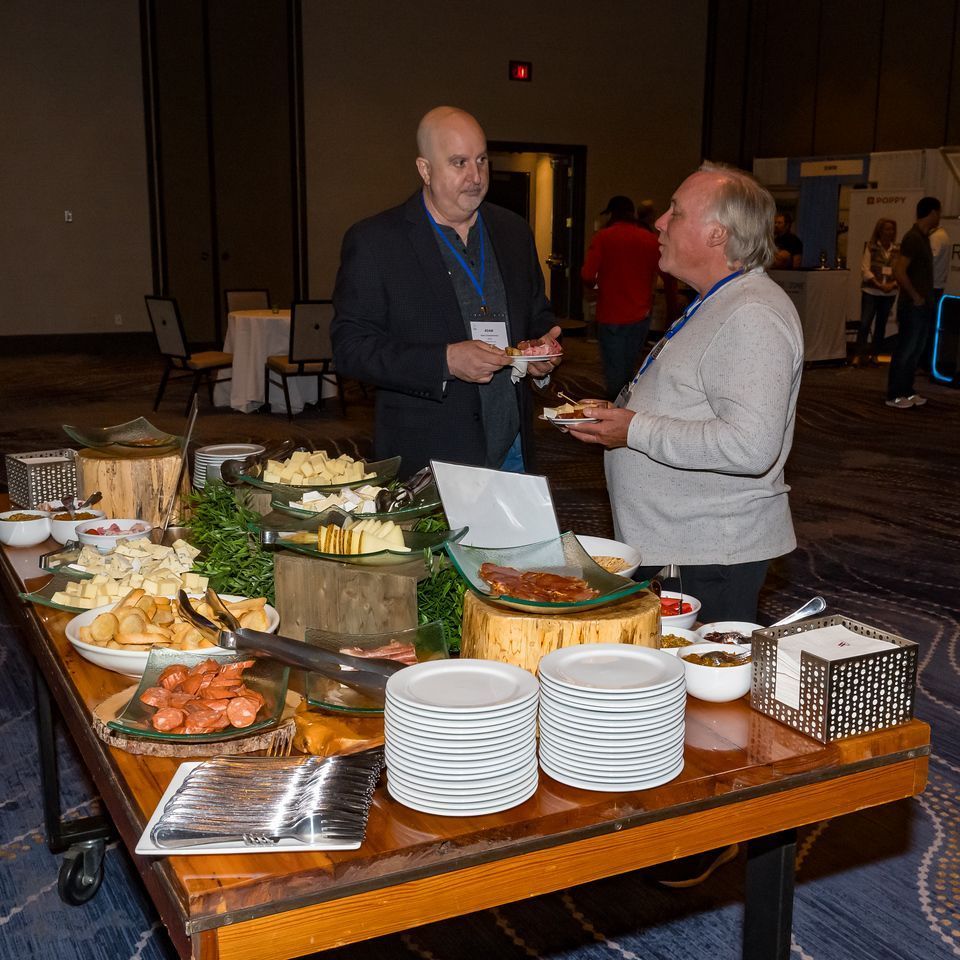 Two men are standing around a table with plates of food on it.